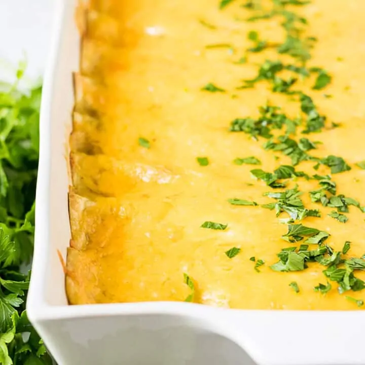 Baking pan full of cheesy breakfast enchiladas topped with chopped parsely.