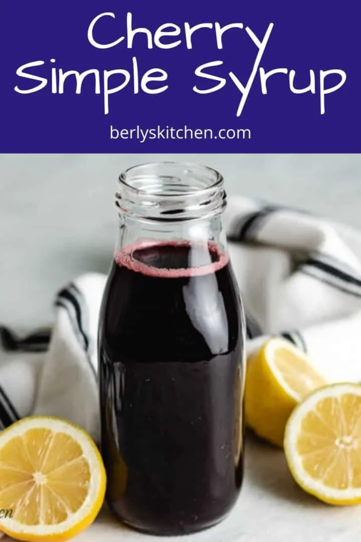 Cherry simple syrup in a bottle surrounded by halved lemons.