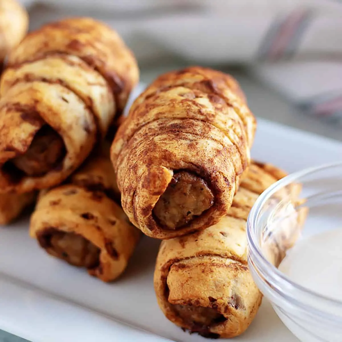 Sausage links rolled in cinnamon rolls sitting on a platter.