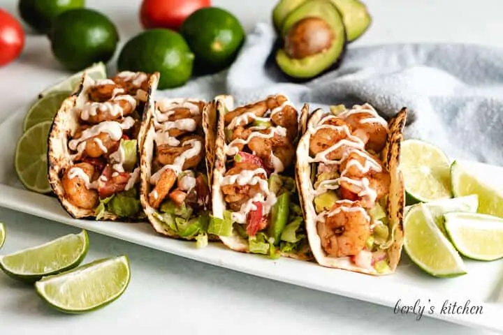 Four shrimp tacos with chipotle sauce on a rectangular platter.