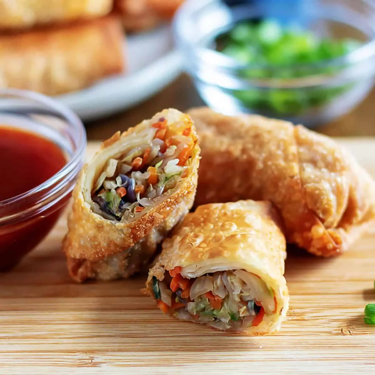 Three egg rolls stacked on a wooden board.