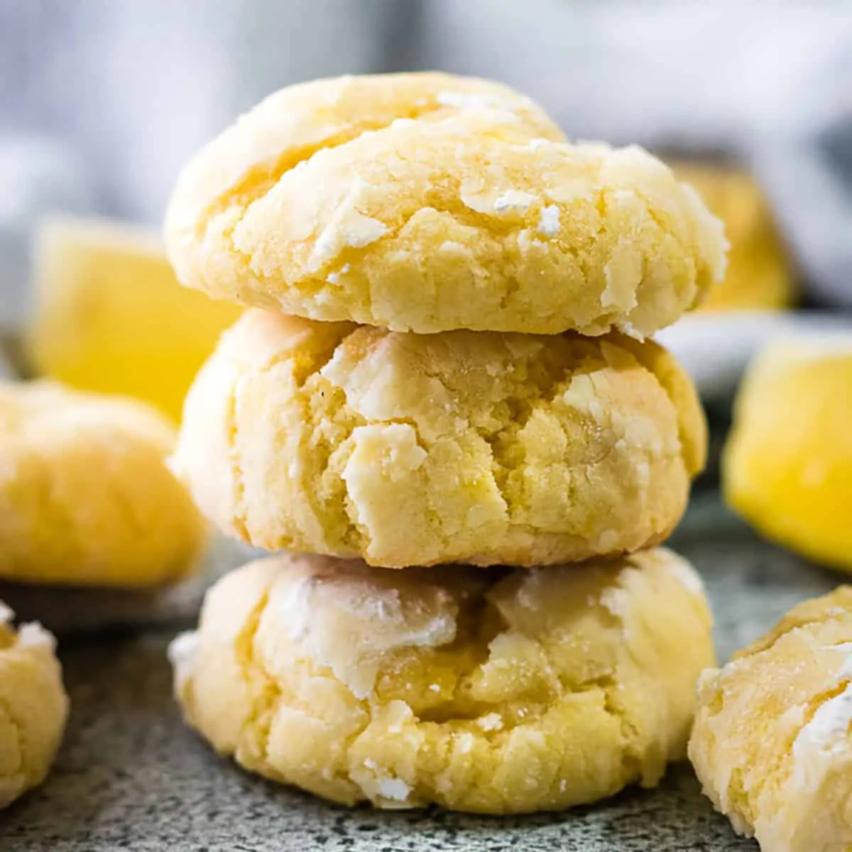 Stack of lemon crinkle cookies next to fresh lemons.