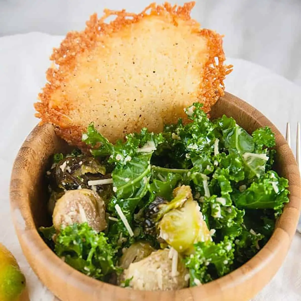 Close up of a bowl of roasted brussel sprouts caesar salad with a parmesan crisp.