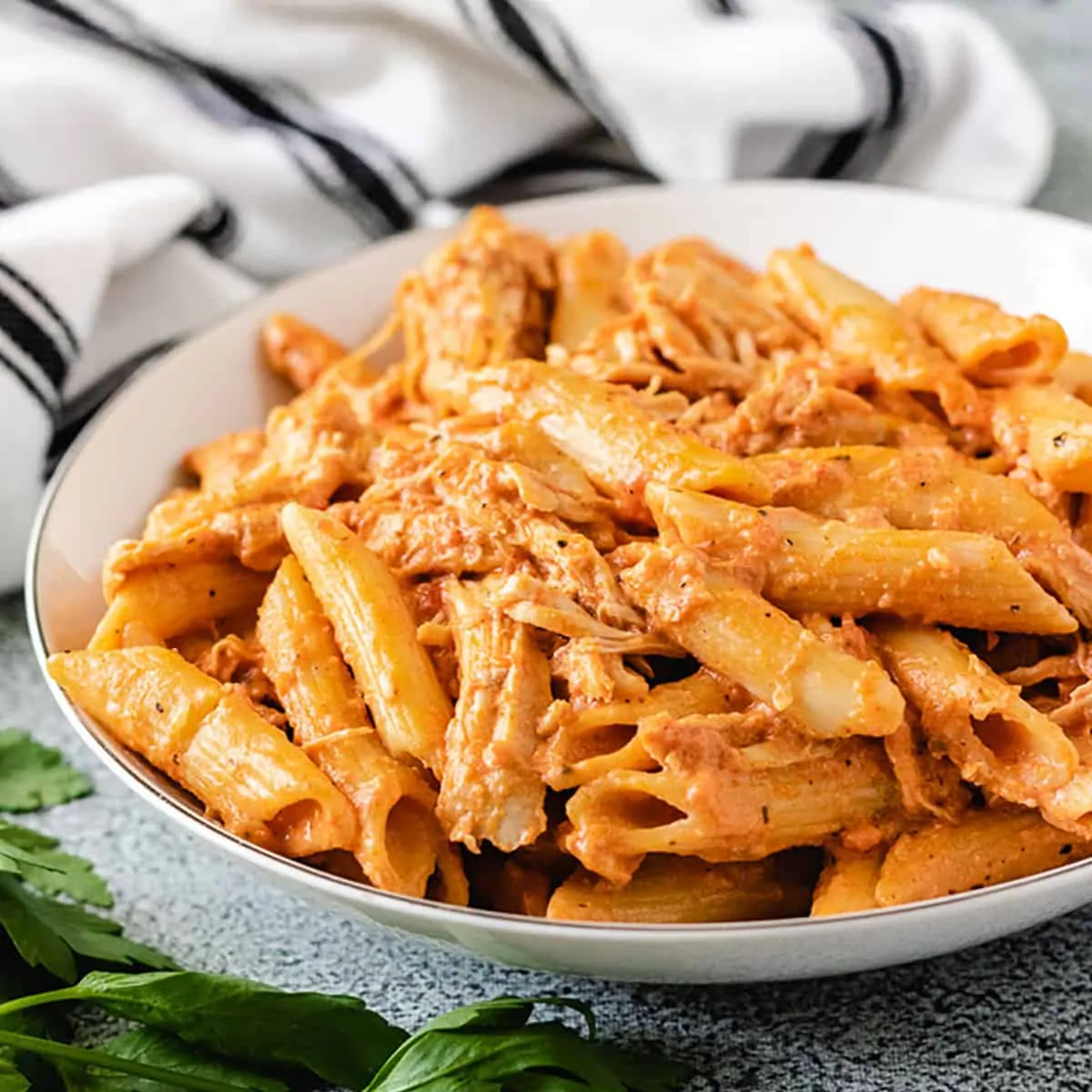 Plate of creamy chicken tomato pasta next to a blue and white striped towel.