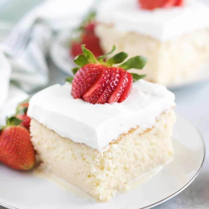 A slice of tres leches cake topped with strawberries on a plate.
