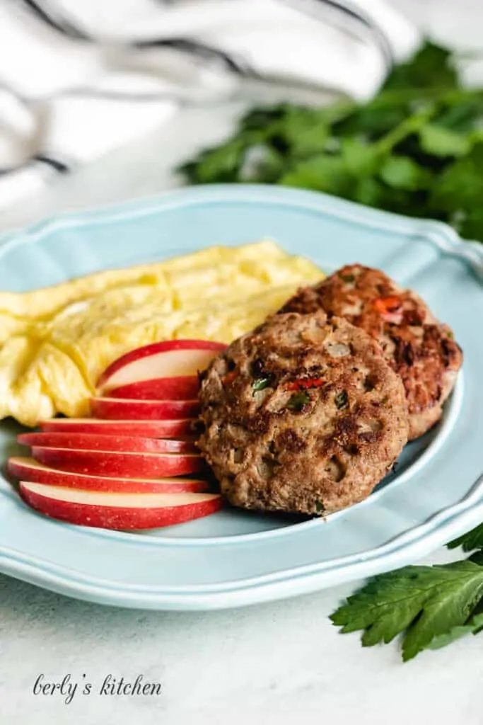 A blue plate with the cooked sausage, sliced apples, and scrambled eggs.