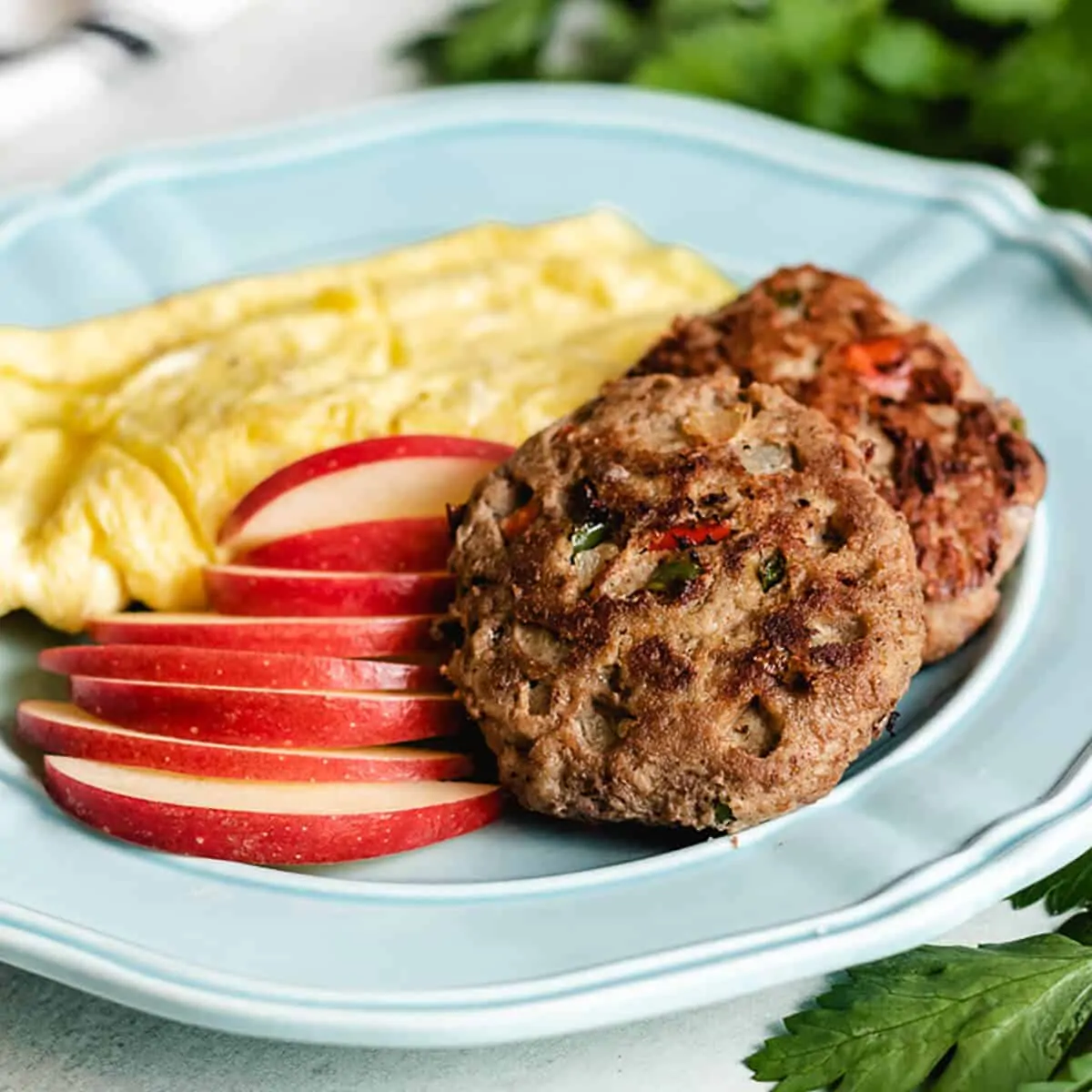 Two cooked turkey sausage patties served with sliced apples and scrambled eggs.