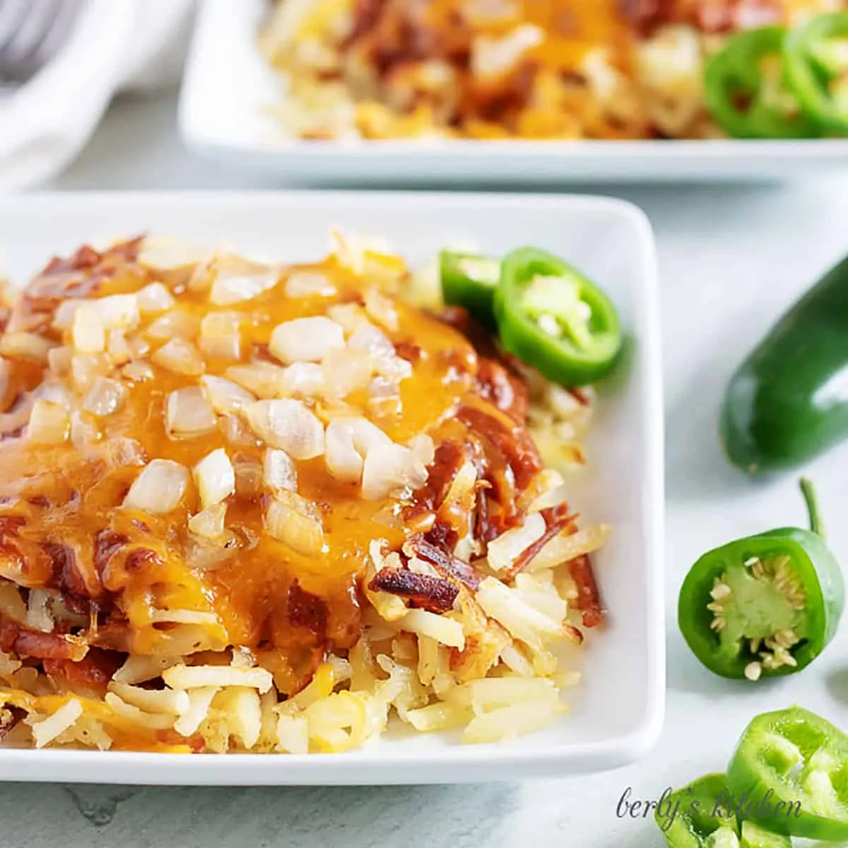 Plate of hash browns covered with chili, cheese, and diced onions next to sliced jalapenos.