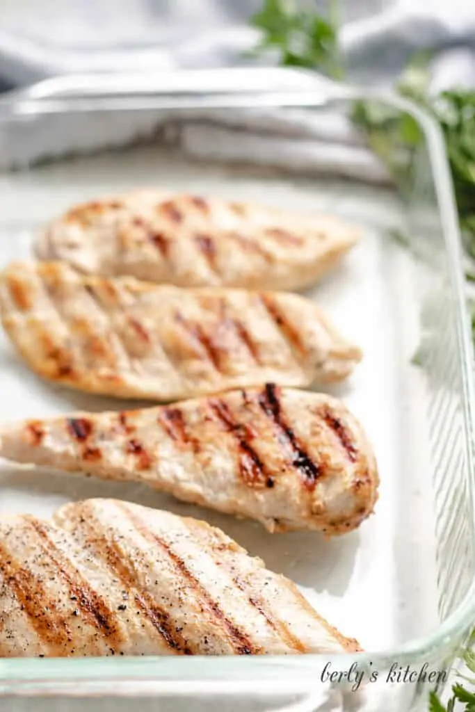 Four chicken breast cutlets in a large baking dish.