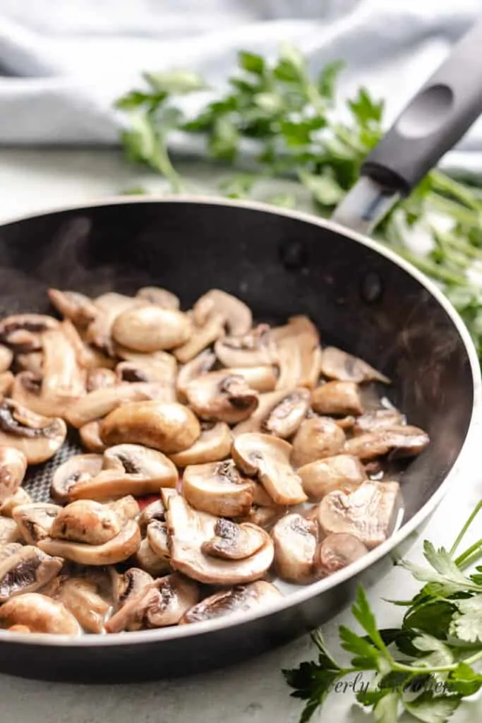 Mushrooms being sauteed in a pan with butter.