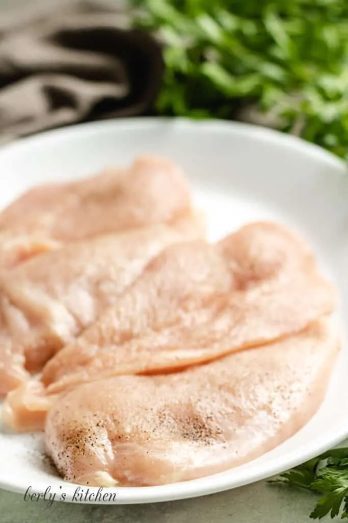 Raw seasoned chicken breast on a plate.