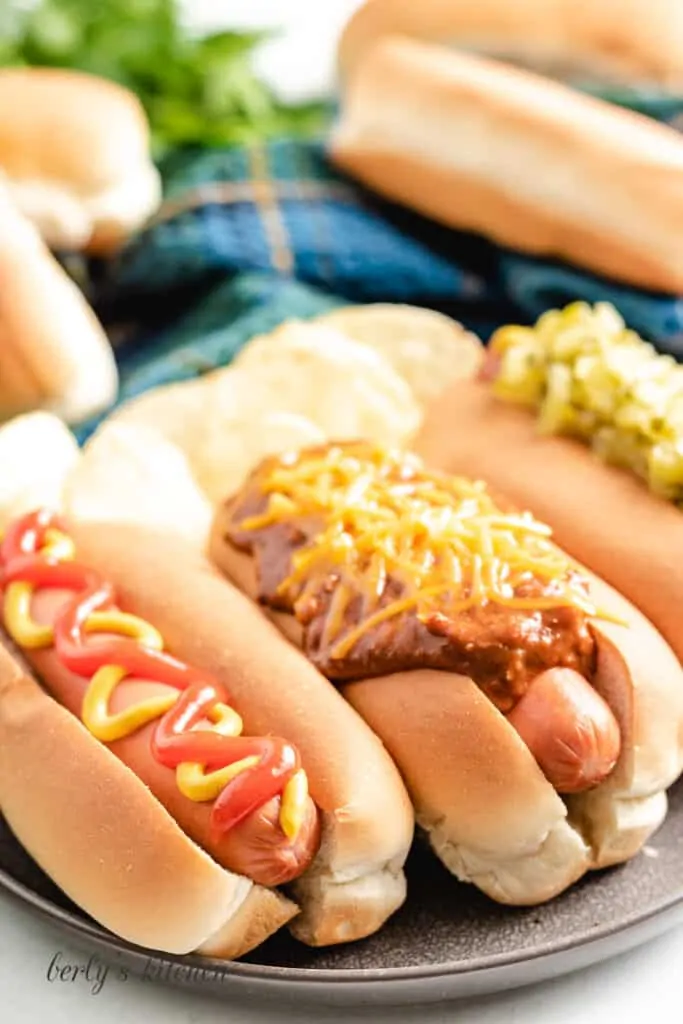 Three cooked sausages in buns with toppings.