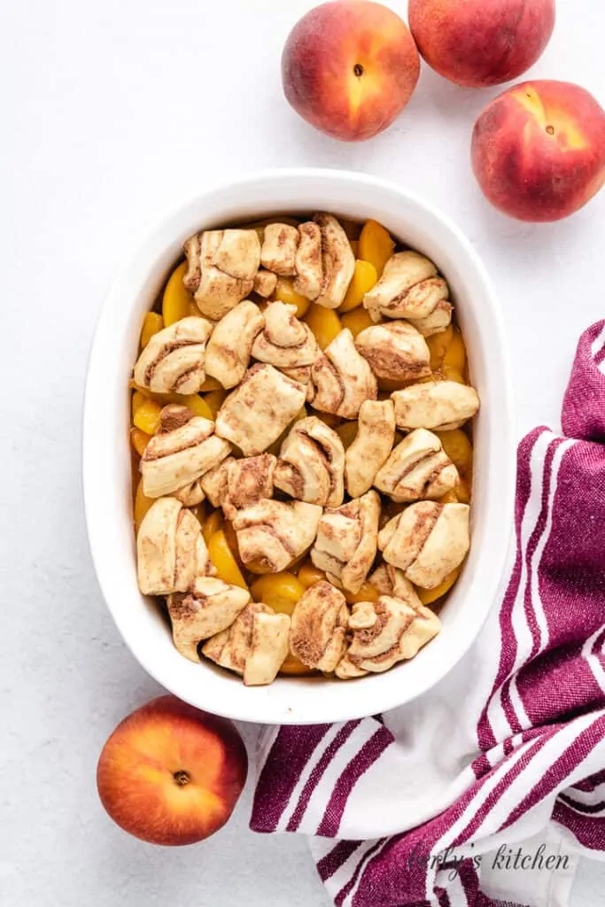 The cinnamon roll dough placed over the peaches.