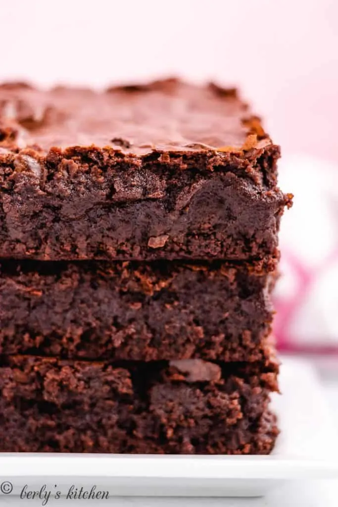 Three fudgy brownies stacked on a plate.