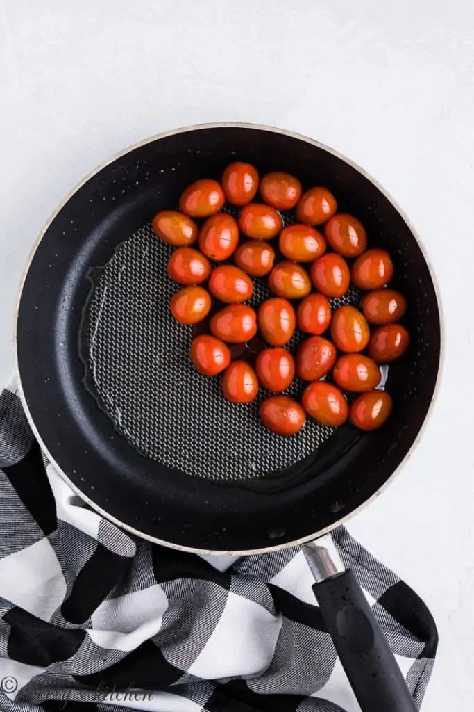 Cherry tomatoes cooking in a saute pan.