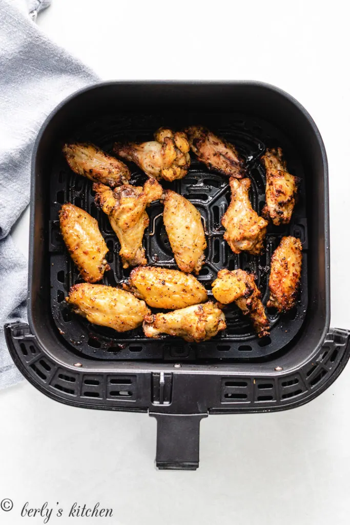 Chicken wings in an air fryer basket.