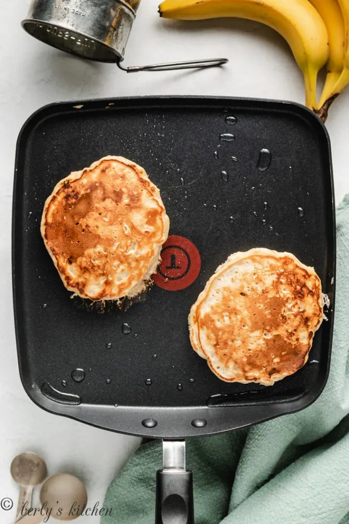 Two pancakes on a griddle.