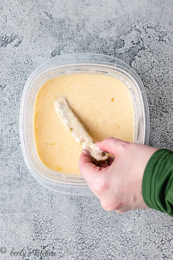 Top down view of a pickle spear being dipped in buttermilk mix.