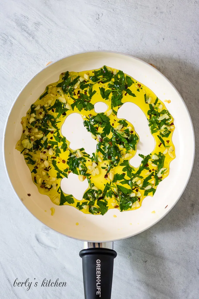 Olive oil, garlic, and other ingredients sautéed in a pan.