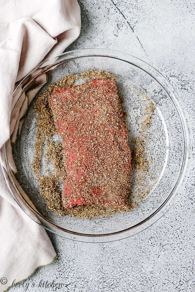 Top down view of flat iron steak in a dish with seasoning.