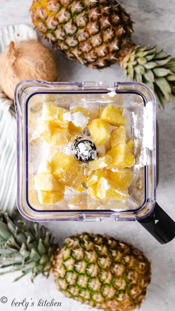 Top down view of pineapple and coconut milk in a blender.