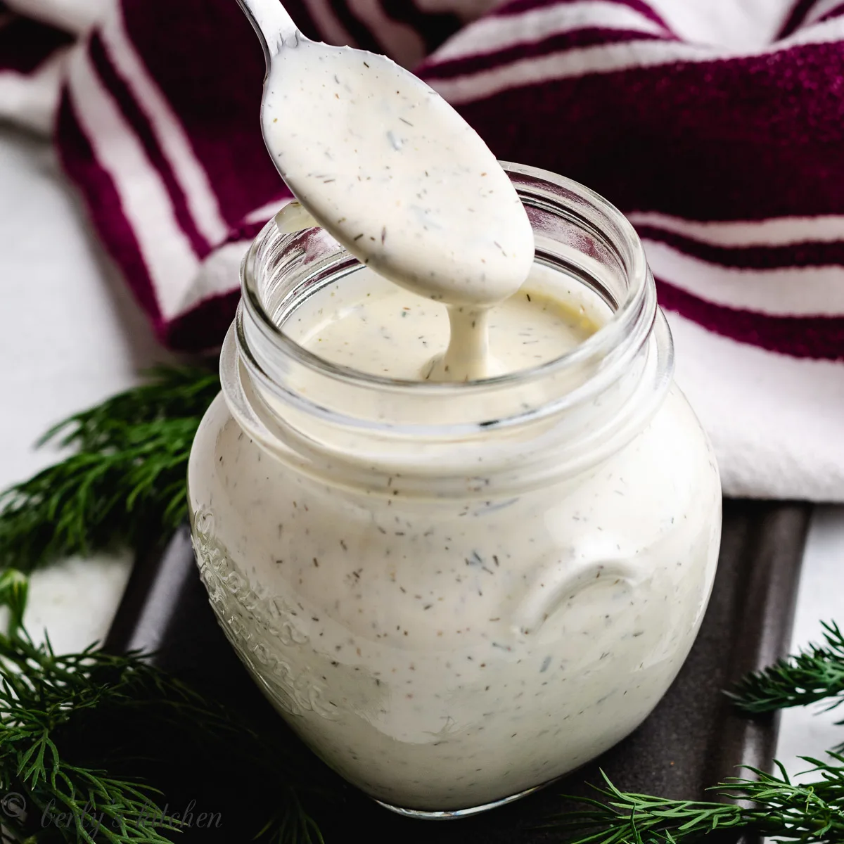 Mason jar with a scoop of dill pickle dressing on a spoon.