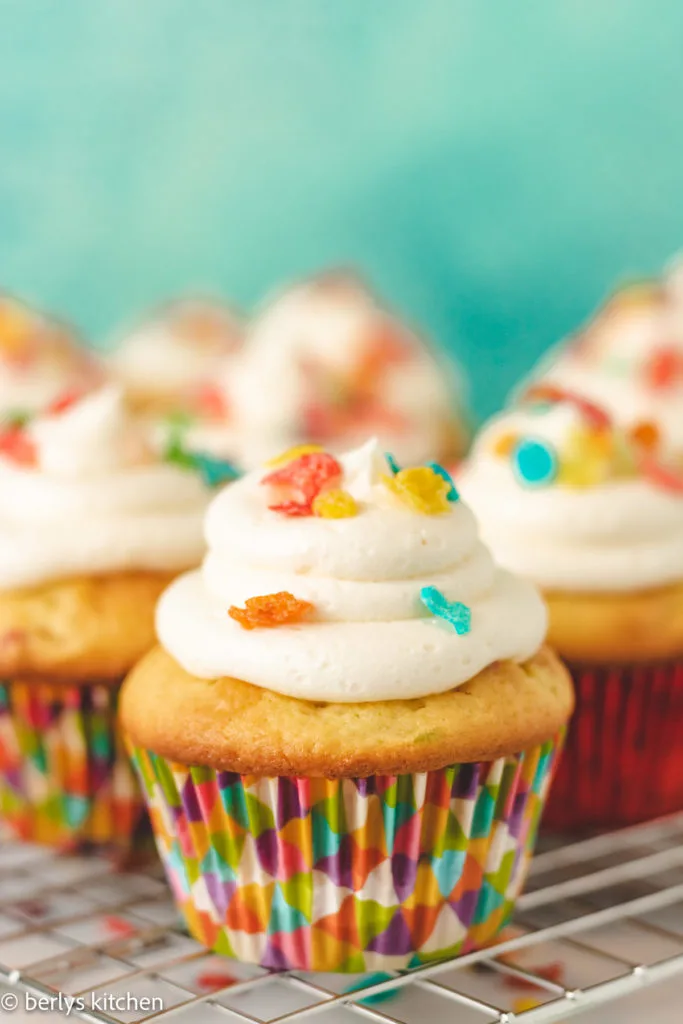 Fruity pebbles cupcakes on a wire rack.