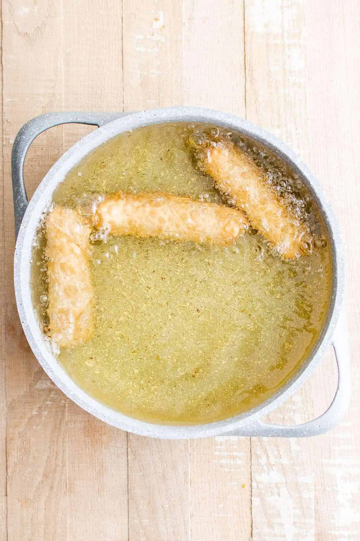 Top down view of egg rolls frying in a pan.