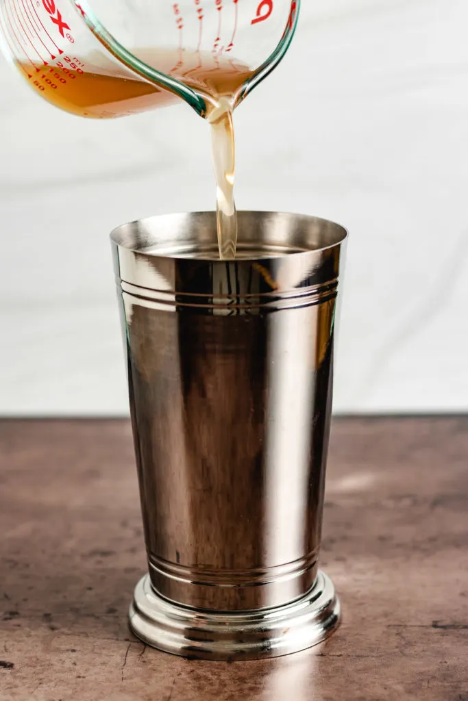 Apple cider being poured into a drink shaker.