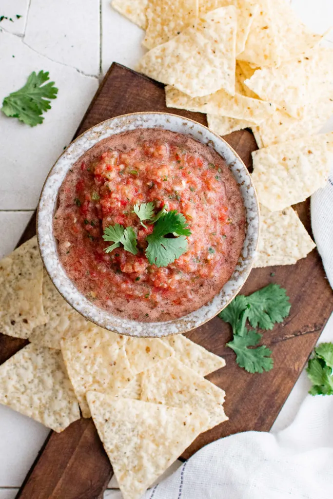 Top down view of chips, salsa, and cilantro on a cutting board.