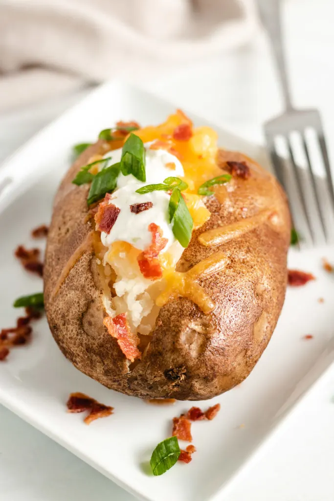 Top down view of a loaded baked potato on a square plate.