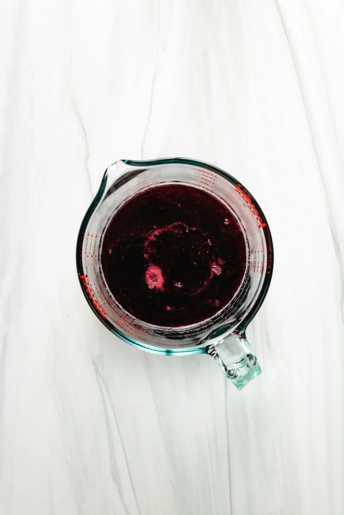 Top down view of strained blackberry syrup in a measuring cup.