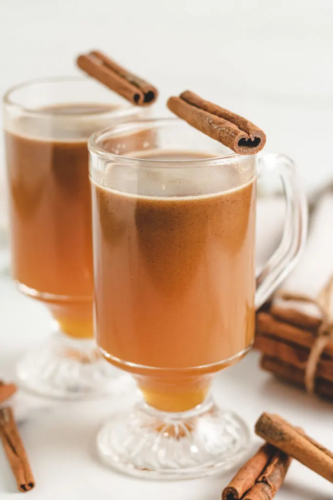 Side view of apple cider and rum in two glass coffee mugs.