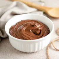 White dish filled with frosting and a wooden spoon.