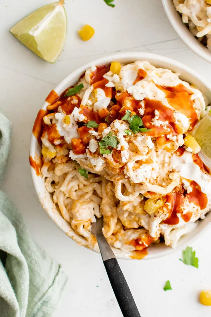 Top down view of elote ramen with hot sauce and crema in a bowl.