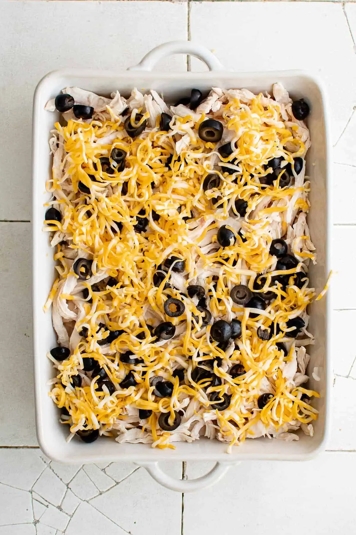 Top down view of creamy filling, chicken, olives and cheese in a pan.