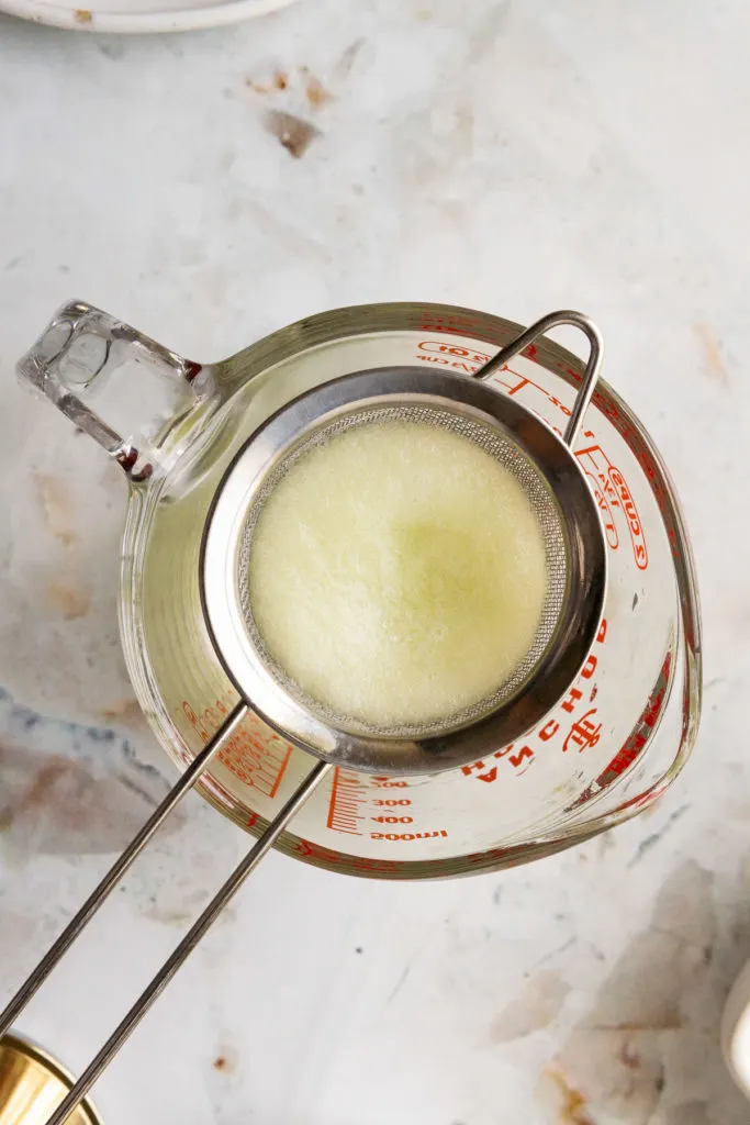 Cucumber juice being poured through a strainer.