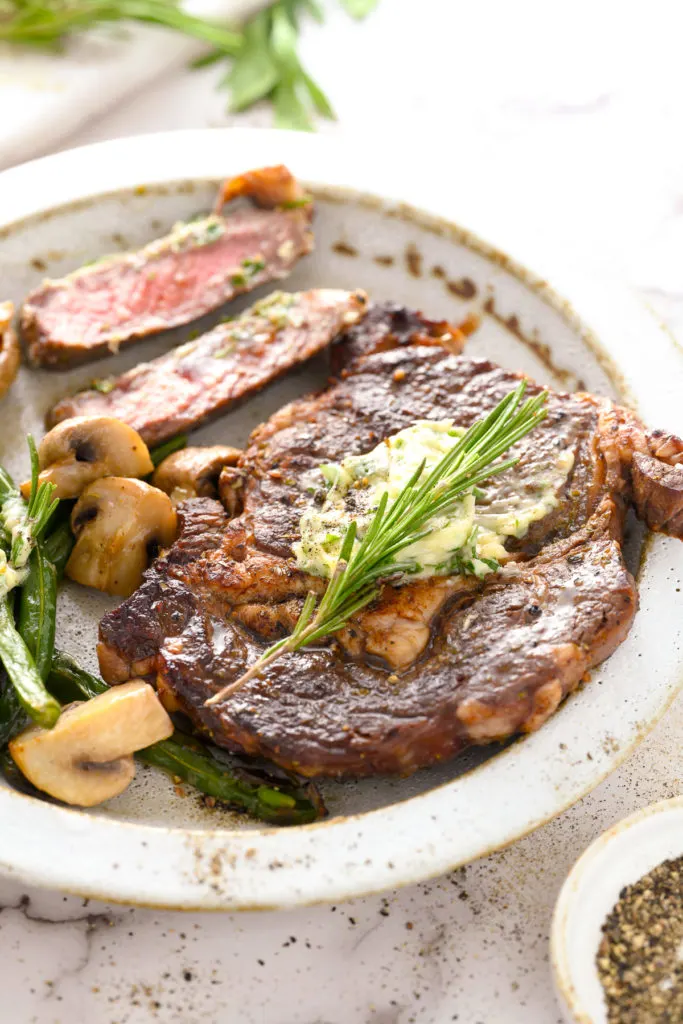 Side view of a steak with herb compound butter.