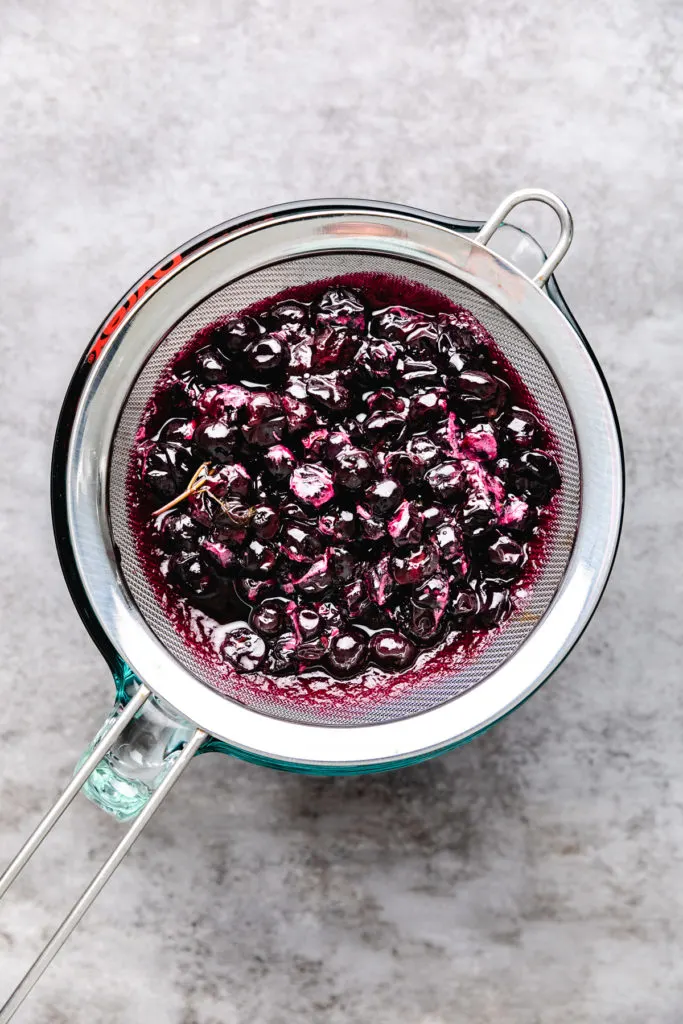 Blueberry thyme simple syrup poured through a mesh sieve.