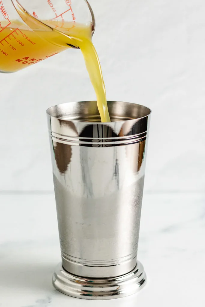 Pineapple juice being added to a drink shaker.