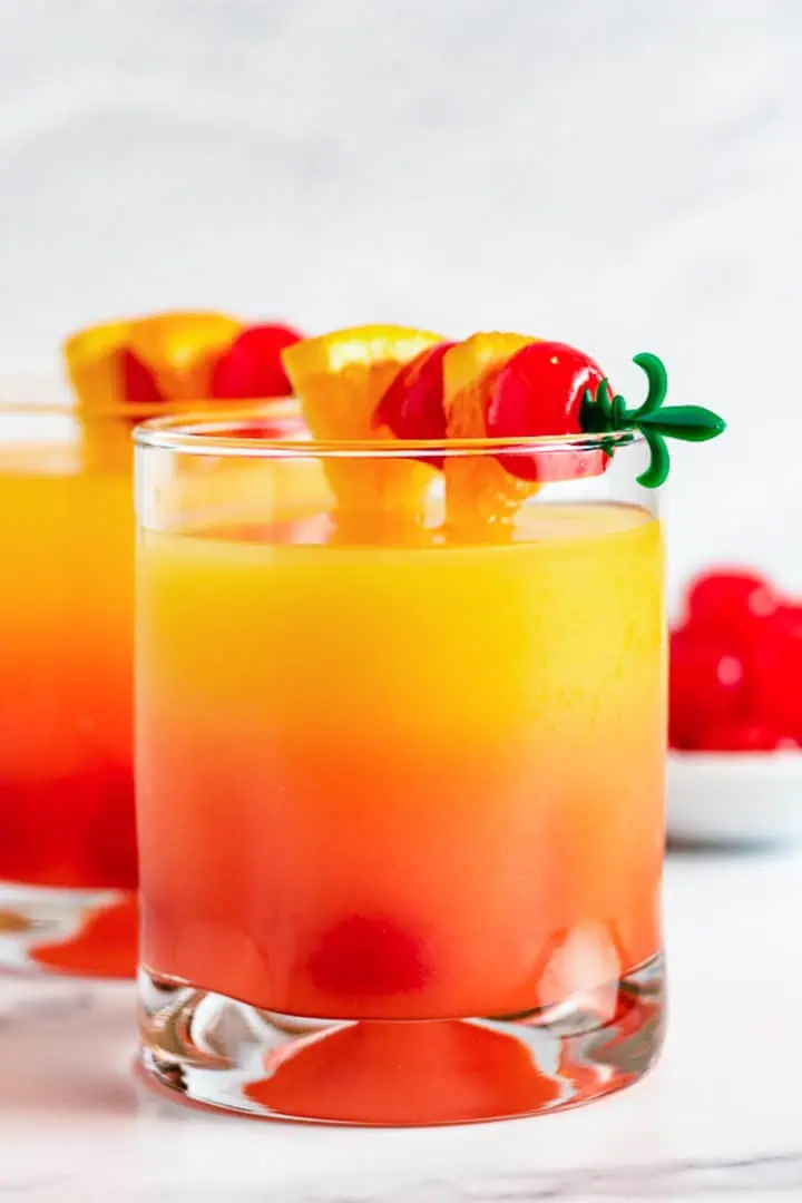 Two rum mixed drinks with orange and cherry garnish.