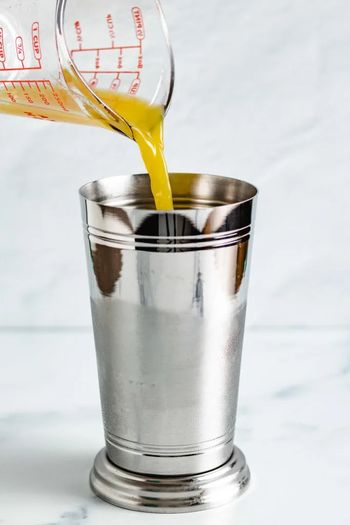 Orange juice being added to a metal drink shaker.