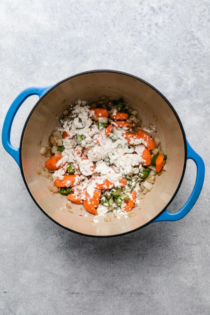 Flour sprinkled over carrots, onions, and celery in a pan.