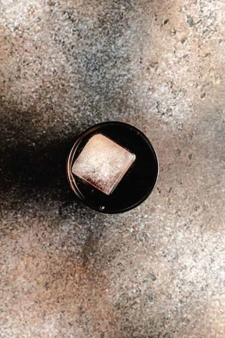 Top down view of a large ice cube in a glass of rum and coke.