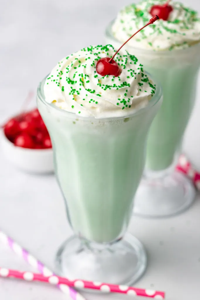 Side view of whipped cream, sprinkles, and cherry on a shake.