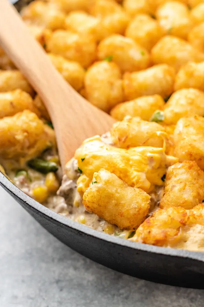 Wooden spoon scooping cheesy potato puff casserole.