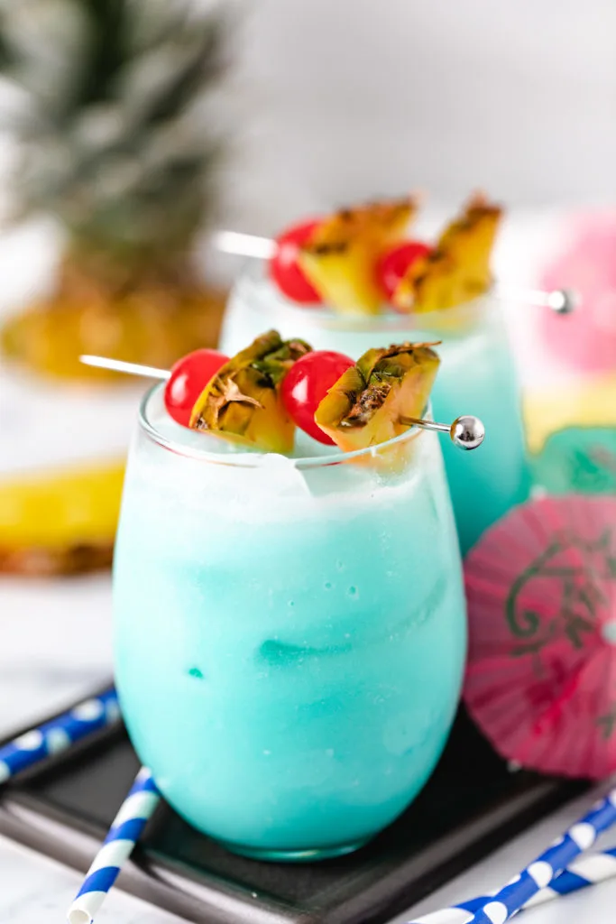 Close up view of a blue hawaiian drink with cherries and pineapple.