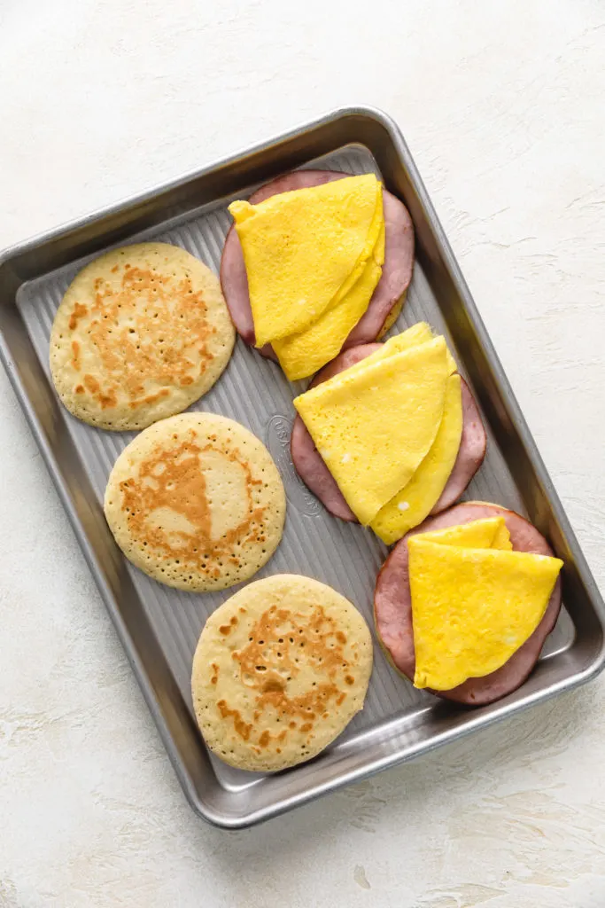 Eggs being added to breakfast sandwiches.