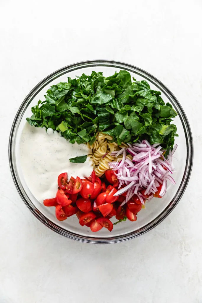 Pasta, lettuce, tomatoes, onions, and ranch dressing in a mixing bowl.