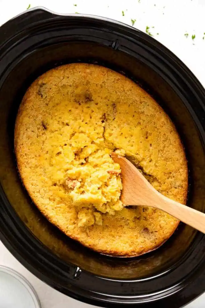 Top down view of a spoon scooping corn casserole from a slow casserole.